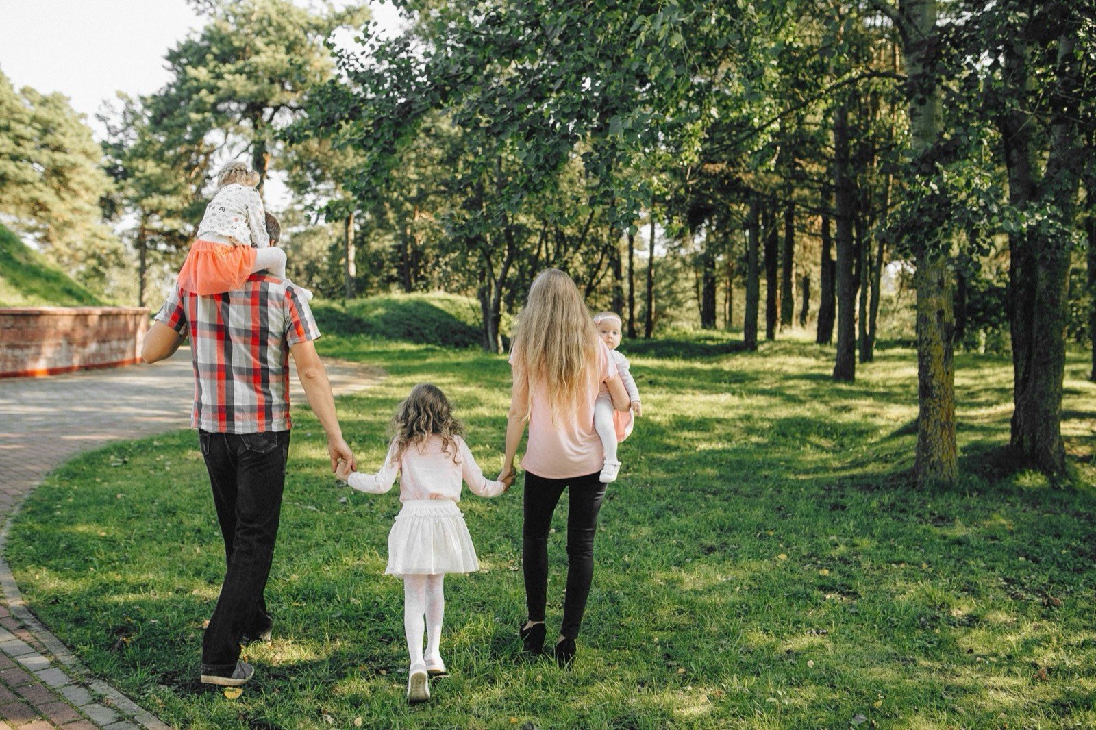 Eltern gehen mit zwei Kindern Hand in Hand durch einen Park.