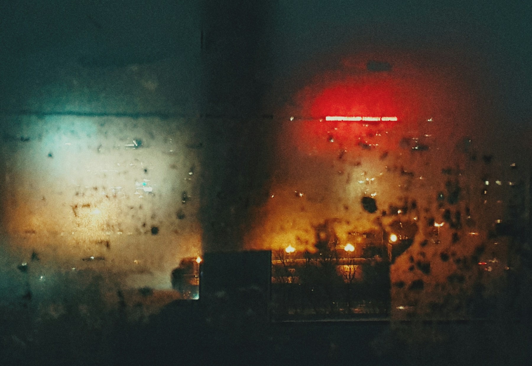 Regentropfen auf einer Fensterscheibe, dahinter Lichter der Stadt bei Nacht