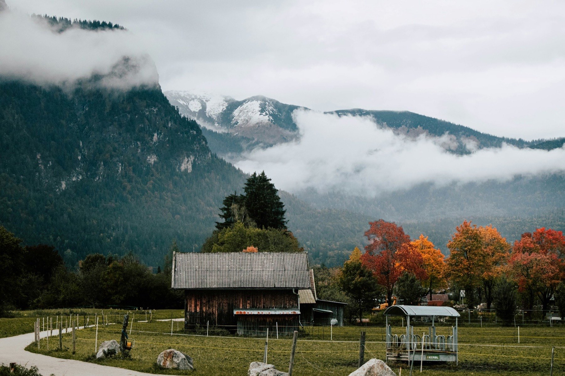Alter Holzstadel auf einer Wiese, dahinter bewaldete Berge im Herbstnebel